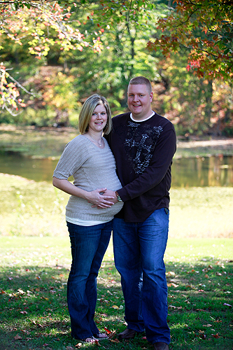 pregnant woman and man posing in park in front of lake